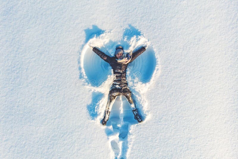 Vue aérienne supérieure de la jeune fille de sourire heureuse faisant par le chiffre d'ange de neige de bras et se situant dans l images stock Vue aérienne supérieure de la jeune fille de sourire heureuse faisant par le chiffre d'ange de neige de bras et se situant dans l images stock