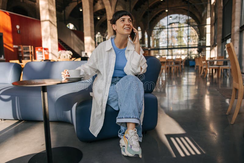 Vue complète de la jeune européenne assise sur l'entraîneur au café avec téléphone photographie stock
