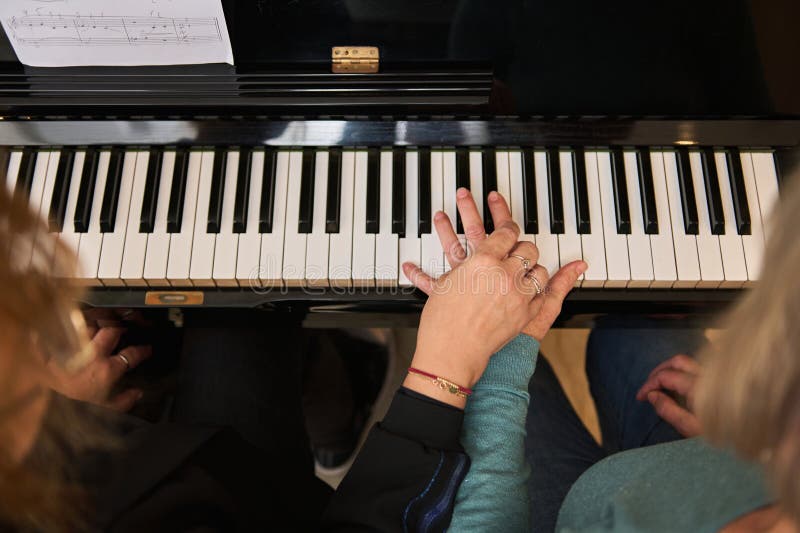 Vue d'en haut femmes se tenant la main en jouant de composition musicale classique sensation de rythme tout en jouant du piano à q. Vue d'en haut femmes tenant la main sur piano ébène et touches blanches exécutant composition musicale classique sensation de rythme tout en jouant piano à la maison. leçons de musique pour adultes. gens. éducation