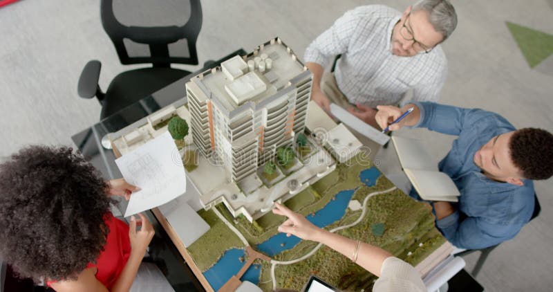 Vue d'ensemble d'une équipe d'ingénieurs divers discutant d'un modèle de bâtiment 3d au bureau clips vidéos