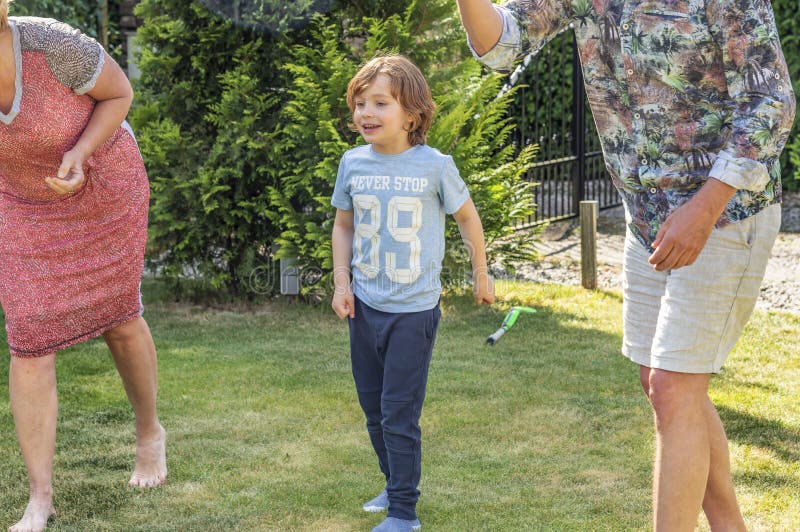 Vue d'un garçon 6 qui attend avec intérêt les adultes de montres de jardin jouant un jeu de boule image stock Vue d'un garçon 6 qui attend avec intérêt les adultes de montres de jardin jouant un jeu de boule image stock