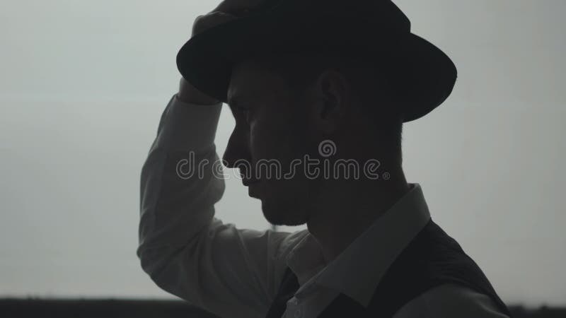 Vue de c? t? de l'homme s? r bel mettant un chapeau sur la t? te devant la grande fen? tre La t? te de la pr? paration de Mafia banque de vidéos