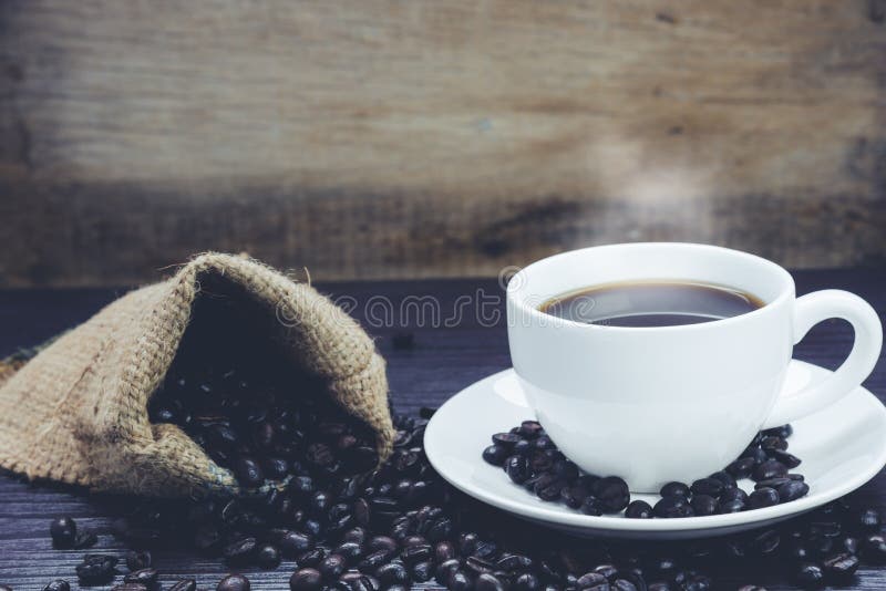 Vue de c?t? de tasse de caf? avec de la fum?e et des grains de caf? dans le sac sur la table en bois, boissons et d?tendre le con images libres de droits Vue de c?t? de tasse de caf? avec de la fum?e et des grains de caf? dans le sac sur la table en bois, boissons et d?tendre le con images libres de droits