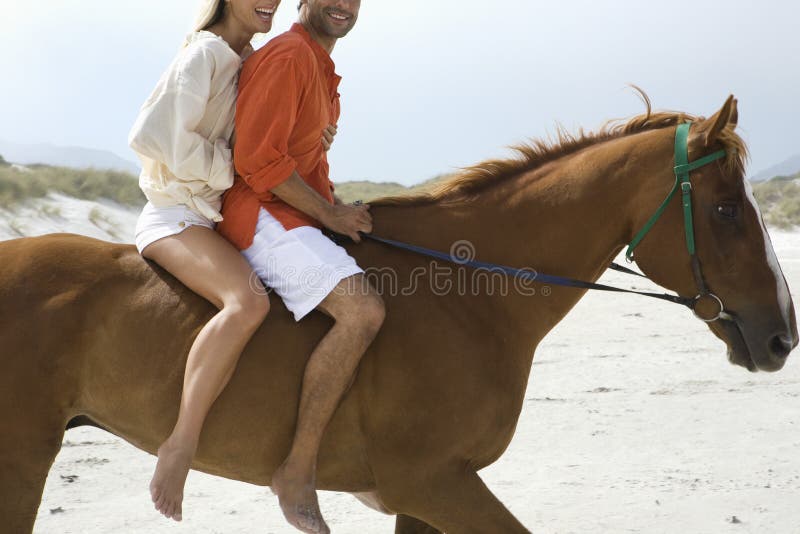 Vue de côté de cheval d'équitation de couples sur la plage photos libres de droits Vue de côté de cheval d'équitation de couples sur la plage photos libres de droits