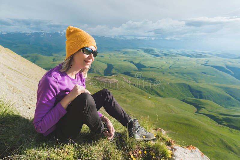 Vue de côté d'une position de touristes femelle attrayante sur les lunettes de soleil de port d'une colline herbeuse Appréciant u images stock Vue de côté d'une position de touristes femelle attrayante sur les lunettes de soleil de port d'une colline herbeuse Appréciant u images stock