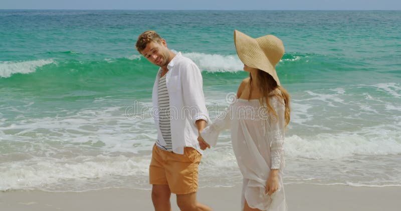 Vue de côté des couples caucasiens marchant de pair sur la plage 4k clips vidéos
