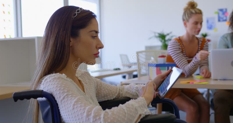 Vue de côté du jeune fonctionnement handicapé caucasien de femelle sur le comprimé numérique dans le bureau moderne 4k banque de vidéos