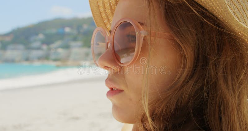 Vue de côté de femme caucasienne dans le chapeau détendant sur la plage 4k banque de vidéos