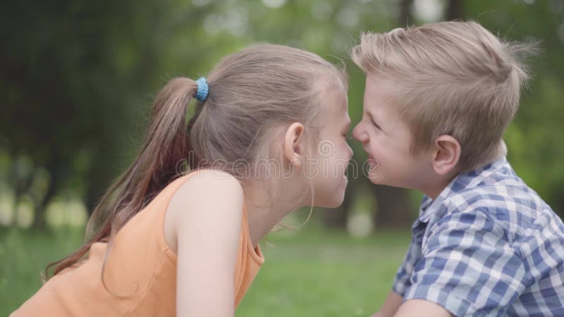 Vue de côté de garçon mignon et de fille s'asseyant en parc, frottant leurs nez et ayant l'amusement Quelques enfants heureux clips vidéos