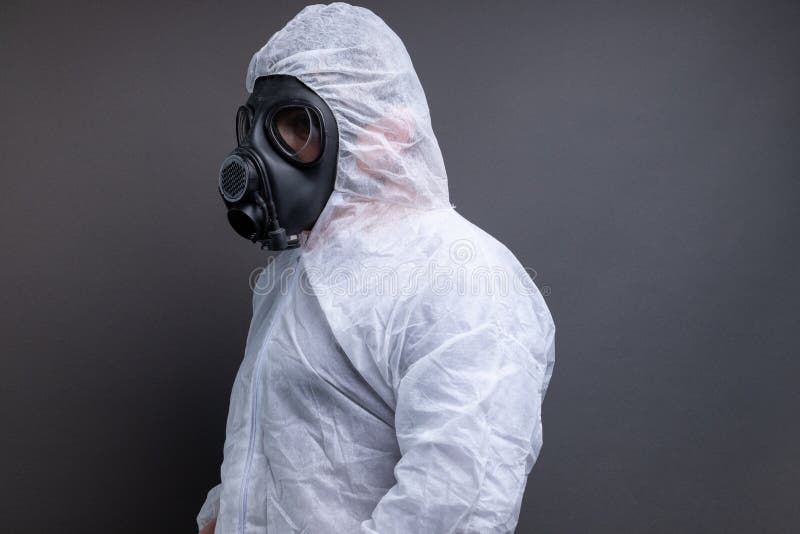 Vue de côté de l'homme avec le masque de gaz dans le costume global protecteur sur le fond gris photos libres de droits Vue de côté de l'homme avec le masque de gaz dans le costume global protecteur sur le fond gris photos libres de droits