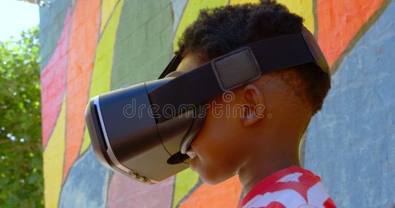 Vue de côté de l'écolier d'Afro-américain à l'aide du casque de réalité virtuelle dans le terrain de jeu 4k d'école banque de vidéos