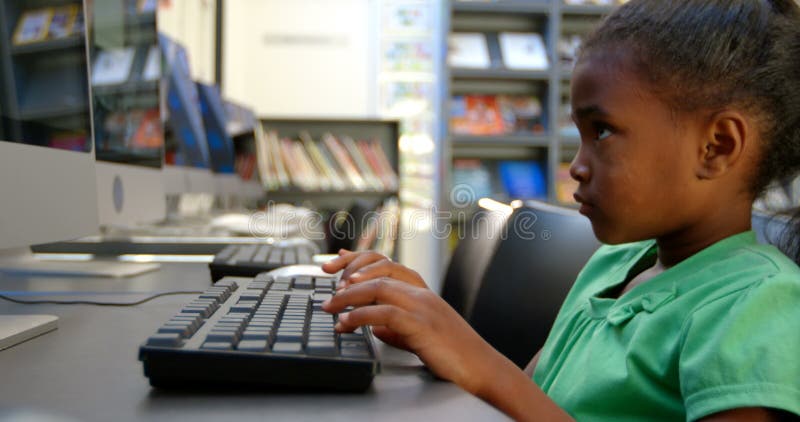 Vue de côté de l'écolière d'Afro-américain à l'aide de l'ordinateur dans la bibliothèque à l'école 4k banque de vidéos