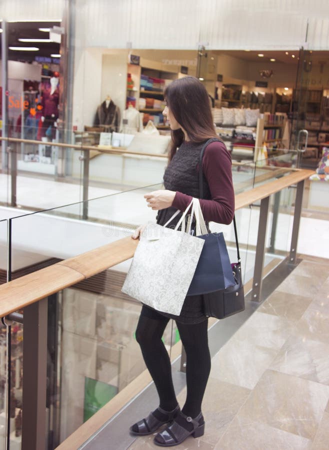 Vue de côté de la femme attirante élégante se tenant dans l'intérieur du centre commercial avec des paniers photos stock Vue de côté de la femme attirante élégante se tenant dans l'intérieur du centre commercial avec des paniers photos stock
