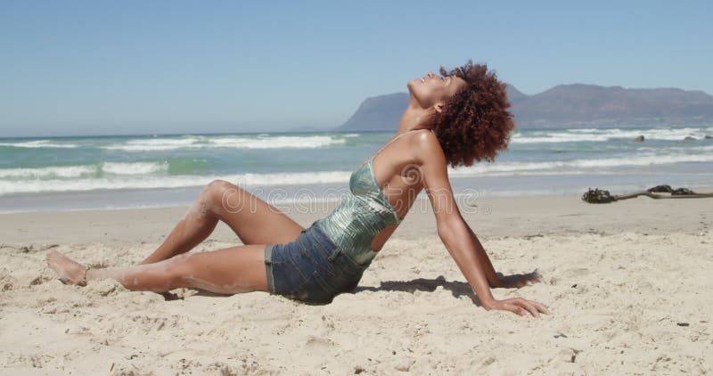 Vue de côté de la jeune femme d'Afro-américain détendant sur la plage 4k banque de vidéos