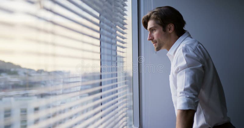Vue de côté de la jeune position exécutive masculine caucasienne réfléchie près de la fenêtre dans le bureau moderne 4k banque de vidéos