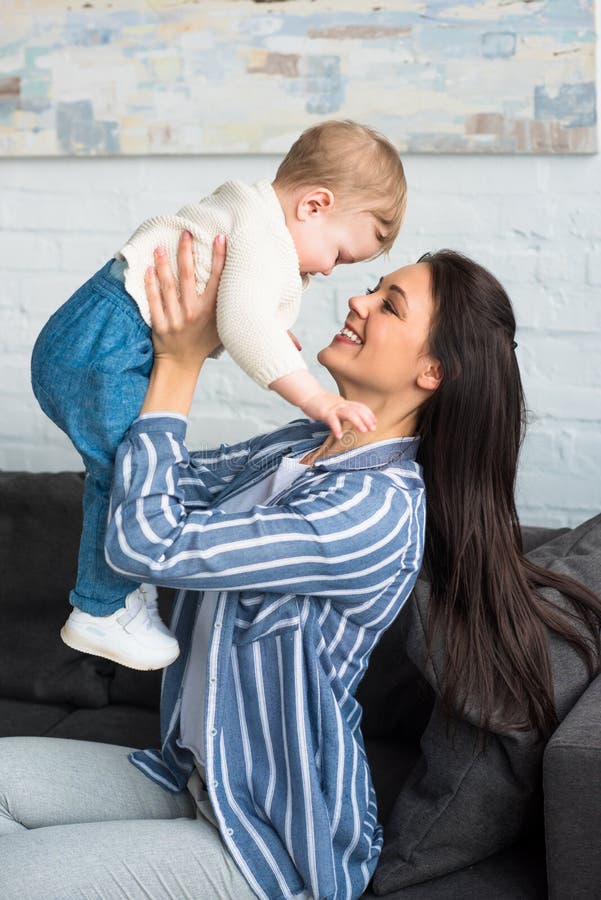 vue de côté de mère heureuse avec le bébé dans des mains se reposant sur le sofa photo libre de droits vue de côté de mère heureuse avec le bébé dans des mains se reposant sur le sofa photo libre de droits