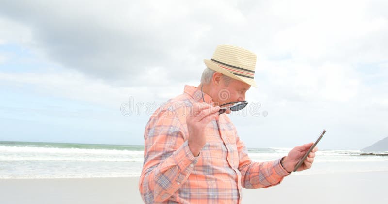 Vue de côté de vieil homme supérieur caucasien utilisant le comprimé numérique à la plage 4k banque de vidéos