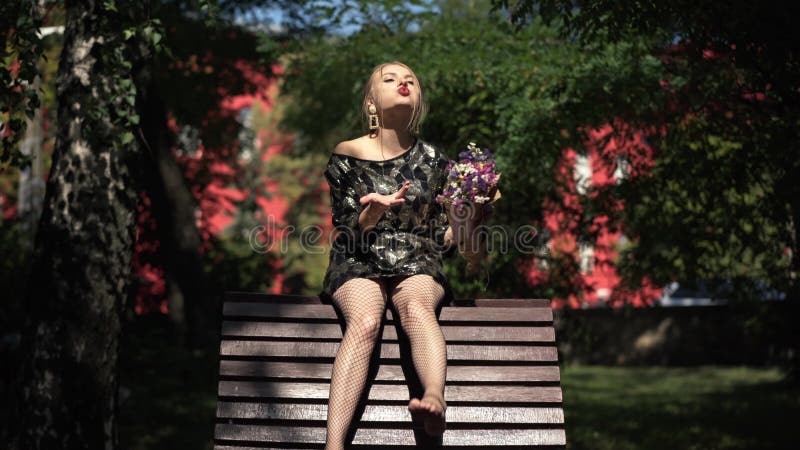 Vue de devant ivrogne rire jeune femme assise sur un banc à la lumière du soleil déchirant des fleurs pétales. portrait de caucasi banque de vidéos