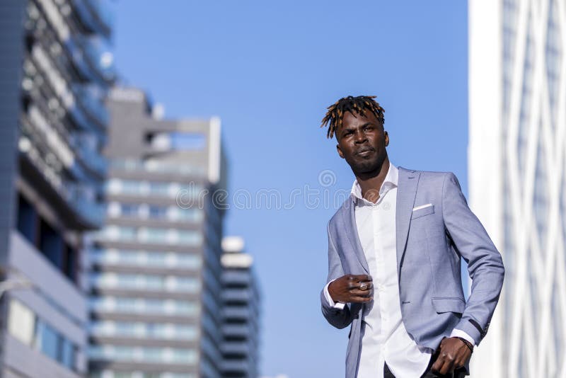 Vue de face d'un homme d'africain noir portant les vêtements élégants se tenant dans la rue tout en regardant loin dans le jour e photographie stock
