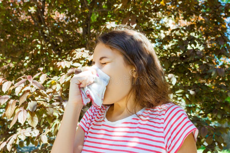 Vue de face d'une fille simple éternuant et soufflant dans un chiffon dehors avec un fond vert photos stock Vue de face d'une fille simple éternuant et soufflant dans un chiffon dehors avec un fond vert photos stock