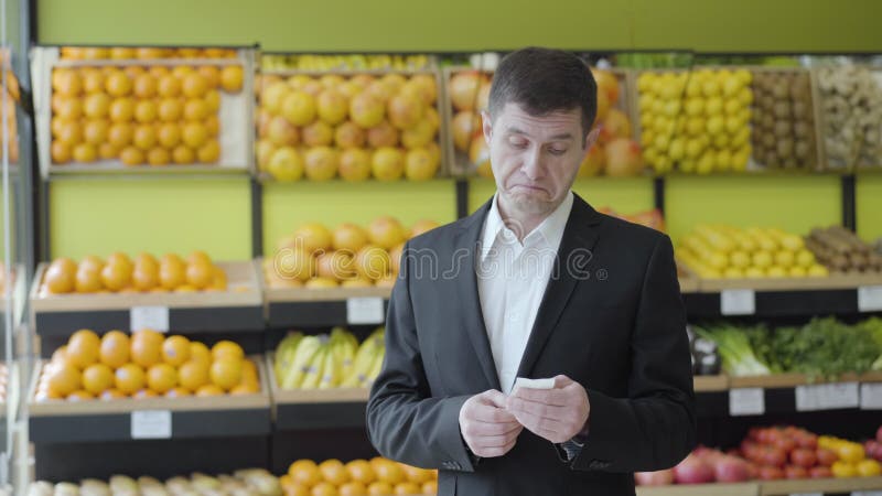 Vue de face de l'homme adulte caucasien vérifiant la facture en épicerie avec l'expression du visage surpris. Portrait de type sér banque de vidéos