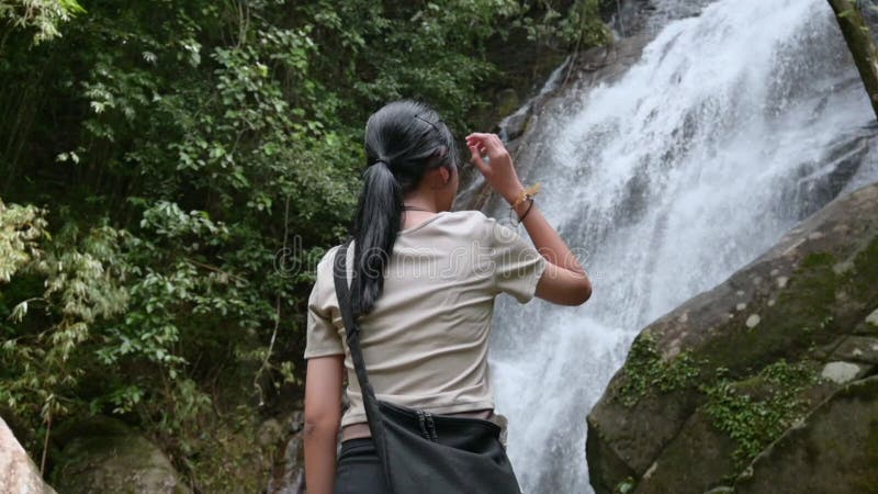 Vue de l'arrière de l'asiatique adolescente profiter avec beau paysage de cascade dans la forêt tropicale. poursuite extérieure. banque de vidéos