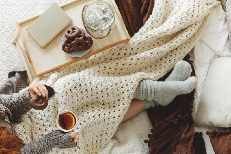 Vue de la jeune fille recouverte d'une confortable couverture blanche assise sur le lit, buvant du thé et mangeant