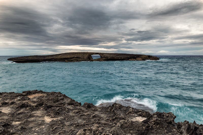 Vue de mer de point de Laie de la roche avec un trou avant coucher du soleil avec le ciel gris-foncé image libre de droits Vue de mer de point de Laie de la roche avec un trou avant coucher du soleil avec le ciel gris-foncé image libre de droits