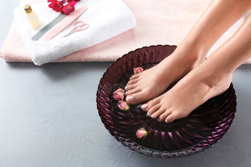 Vue de plan rapproch? de femme imbibant de ses pieds dans le plat l'eau et des roses sur le plancher gris Station thermale - 7 images stock