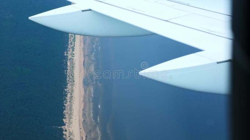 Vue depuis la fenêtre avec l'aile de l'avion. Avion approchant de présenter des vawes d'eau bleue zones forestières vertes et long banque de vidéos