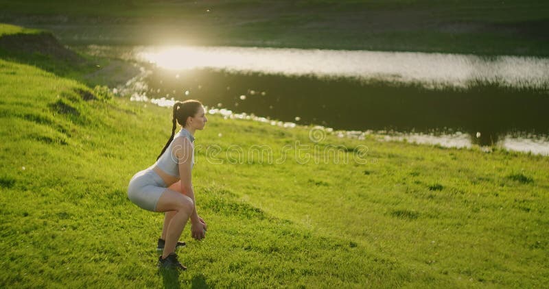 Vue du côté. Une femme exécute des postures accroupies avec des haltères. D'une belle la séance d'exercice femme le matin dans un