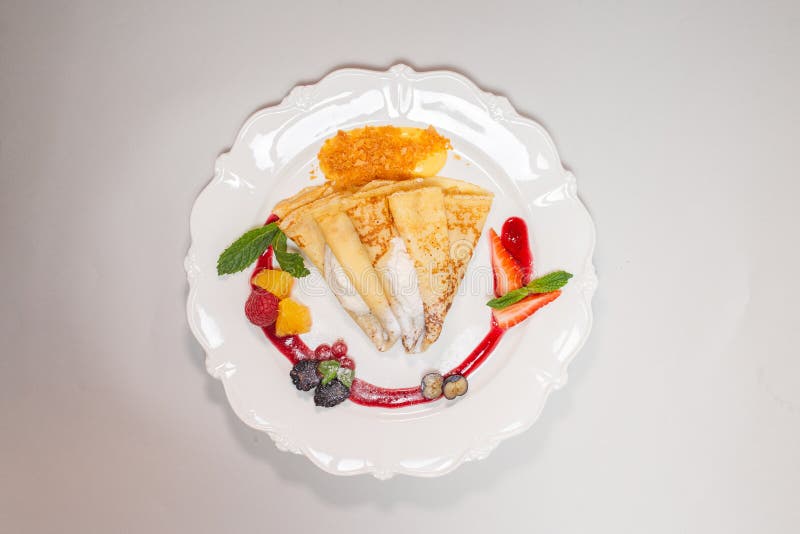 Isolated image of a gourmet pancake on a white plate with red sauce and berries, perfect for food blogs or recipe websites. Isolated image of a gourmet pancake on a white plate with red sauce and berries, perfect for food blogs or recipe websites.