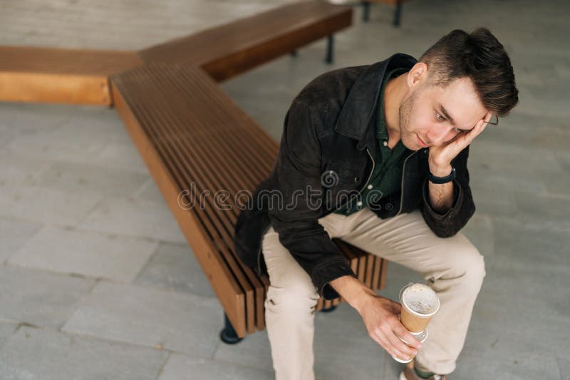 Vue en surplomb de l'homme pensif frustré assis sur le banc de rue tenant une tasse de café et se reposant la tête perdue dans photo libre de droits