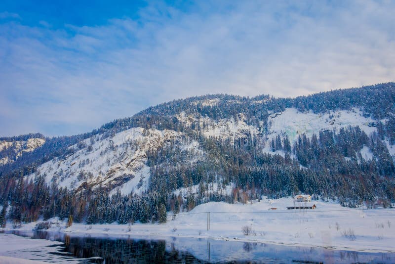 Vue extérieure étonnante de maison en bois près d'un beau lac couvert de neige et de glace dans la forêt pendant l'hiver image stock Vue extérieure étonnante de maison en bois près d'un beau lac couvert de neige et de glace dans la forêt pendant l'hiver image stock
