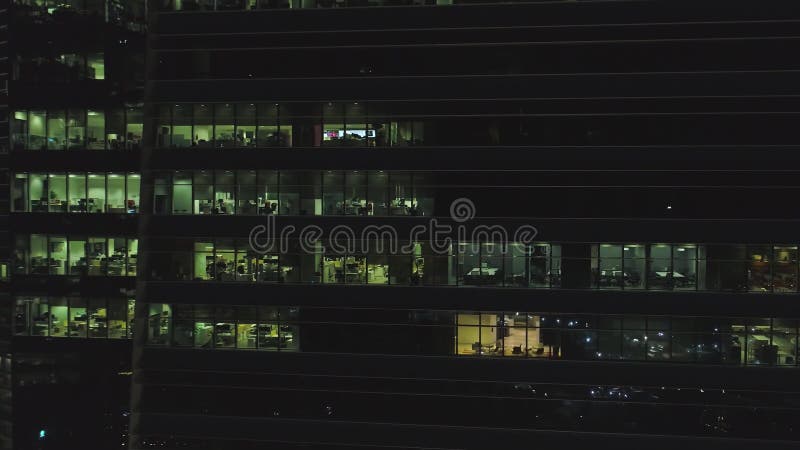 Vue frontale de la façade de nuit du bâtiment avec beaucoup de fenêtres allumées projectile Façade le bâtiment à plusiers étages banque de vidéos