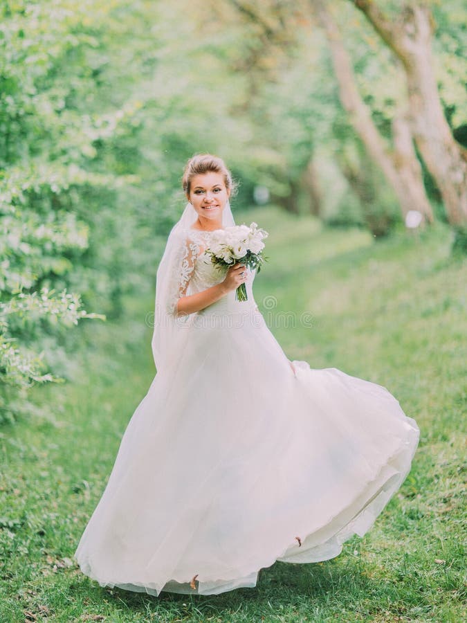 Vue intégrale de la jeune mariée de sourire jouant avec la robe de mariage dans la forêt verte images libres de droits