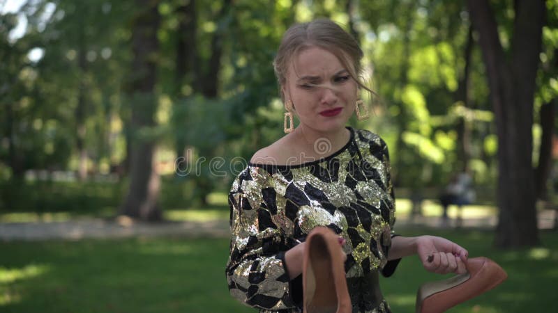 Vue latérale agacée jeune femme agacée avec coeur brisé se promenant dans le parc d'été tenant des talons hauts dans les mains clips vidéos