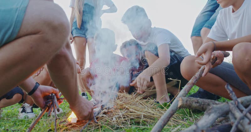 Vue latérale d'enfants assis sur le sol, mettant des branches faisant le feu sourire un garçon debout. groupe d'enfants banque de vidéos