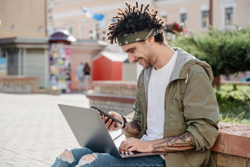 Vue latérale d'un bel homme utilisant un smartphone alors qu'il travaillait sur un ordinateur portable en plein air, un homme heu photos libres de droits