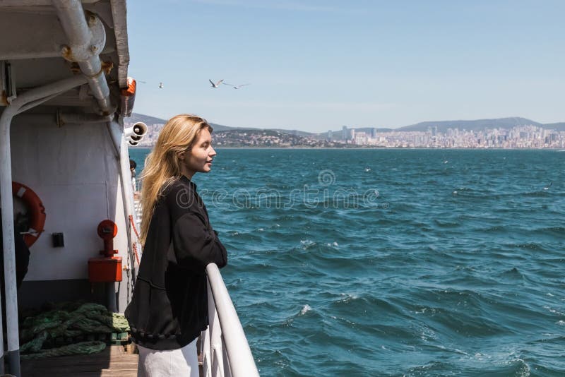 Vue latérale de la femme heureuse dans. Vue latérale d'une femme heureuse en chandail noir regardant la mer à partir du ferry bateau traversant bosporus à istanbul stock image