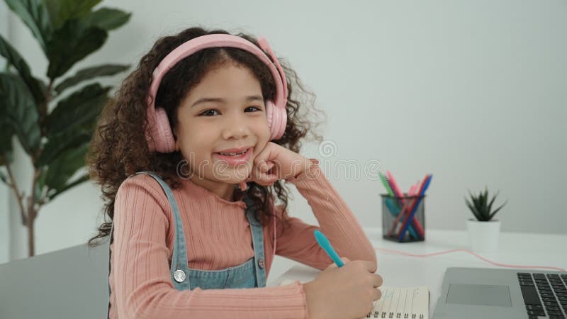 Vue latérale de la fille avec casque faire les devoirs et regarder la caméra. pédagogie. image libre de droits