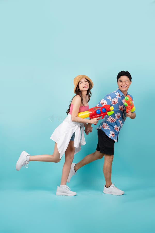 Vue latérale du portrait intégral du jeune couple asiatique marchant et tenant un pistolet à eau isolé sur fond bleu photo libre de droits