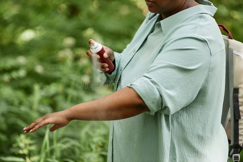 Vue latérale fermeture de la femme noire vaporisant des bras avec insectifuge à l'extérieur images stock