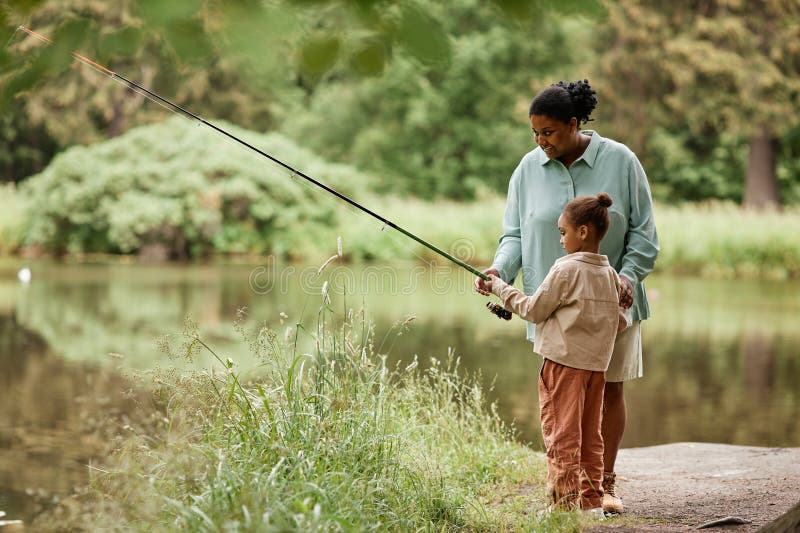 Vue latérale soins mère noire enseignement petite fille pêche photographie stock libre de droits