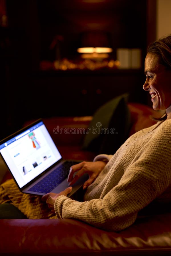 Vue latérale sur la femme à la maison assise dans le salon la nuit shopping en ligne