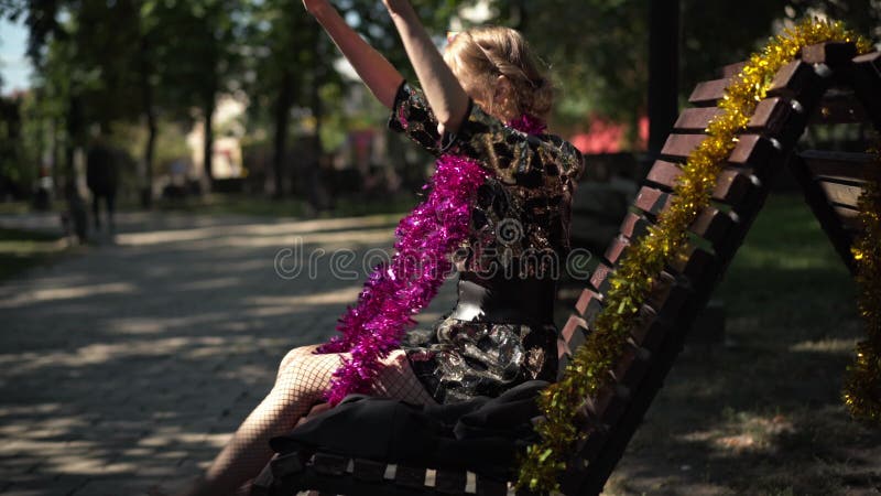 Vue latérale une jeune femme ivrogne chantant assis sur le banc au soleil en enlevant le chapeau de fête. portrait d'agacé irrité banque de vidéos