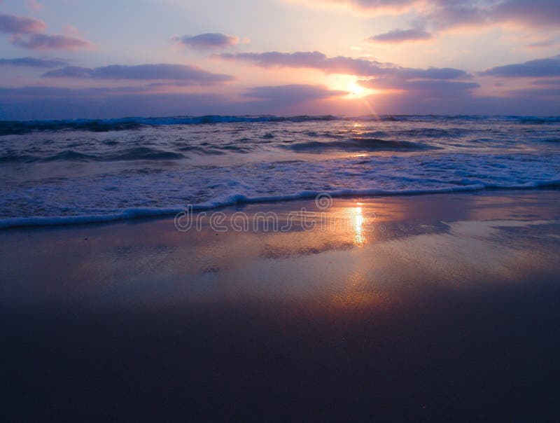 Vue paisible d'un coucher du soleil nuageux sur la plage sablonneuse avec de belles réflexions sur le sable humide image libre de droits Vue paisible d'un coucher du soleil nuageux sur la plage sablonneuse avec de belles réflexions sur le sable humide image libre de droits