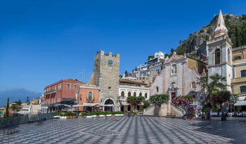 Panoramic view of Taormina main square Piazza IX Aprile with San Giuseppe Church, the Clock Tower and Mount Etna Volcano on background - Taormina, Sicily, Italy. Panoramic view of Taormina main square Piazza IX Aprile with San Giuseppe Church, the Clock Tower and Mount Etna Volcano on background - Taormina, Sicily, Italy