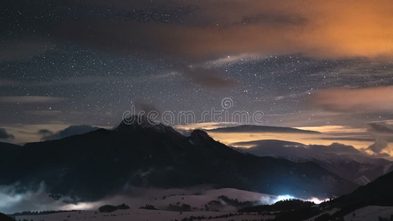 Vue panoramique du ciel étoilé avec des étoiles et des nuages colorés dans les montagnes d'hiver avec de la brume dans les vallées