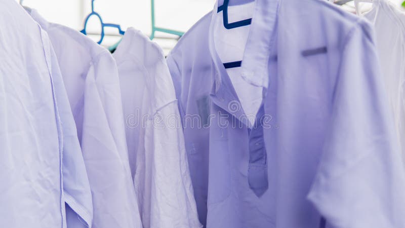 Vue rapprochée de l'uniforme de l'école blanche pour les élèves qui s'asséchent au soleil sur le porte-vêtements en plein air image libre de droits Vue rapprochée de l'uniforme de l'école blanche pour les élèves qui s'asséchent au soleil sur le porte-vêtements en plein air image libre de droits